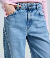 Pantalón de jean estilo baggy con cintura media, corte recto y holgado. Presenta un lavado con efecto dirty y detalles de bordados deshilachados verticales en la parte frontal de las piernas. Cuenta con cierre frontal con botón y cremallera, presillas en la cintura y bolsillos funcionales.