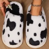 Pantuflas cerradas sin talón con estampado de vaca en blanco y negro, confeccionadas en material afelpado y suela de PVC.