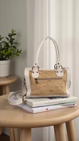 Cartera Diri de cuero natural uruguayo, en tonos marfil y arena, con intervención artística pintada a mano en el frente con pinceladas en rojos, terracotas y dorados. Cuenta con estructura firme, herrajes metálicos en acabado oro viejo, cierres, manijas ergonómicas y correa regulable desmontable.