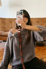 Jersey de punto color marrón topo, con cuello drapeado decorado con un broche metálico dorado y mangas largas de corte holgado.