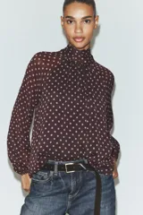 Blusa de cuello subido con diseño de lunares, manga larga abullonada con puños elásticos y forro interior.