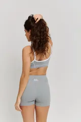 Conjunto deportivo compuesto por un top y un short de tiro alto en color gris. El top presenta breteles blancos y logo estampado en el frente, mientras que el short cuenta con costuras laterales en contraste blanco.