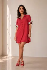 Vestido corto camisero de lino color rojo, con cuello polo, escote en V con botones frontales, mangas cortas con vuelta gris y lazo decorativo, y bolsillos laterales.