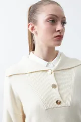 Sweater de tejido de punto color azul marino, con cuello polo amplio y cierre frontal con tres botones metálicos. Presenta mangas largas levemente acampanadas y un diseño de silueta relajada con aberturas laterales en el ruedo.