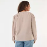 Blusa de corte fluido con estampado de cuadros vichy en tonos beige y blanco. Presenta cuello mao con cordón ajustable terminado en borlas y mangas largas abullonadas con puños elásticos.