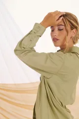 Camisa verde militar de corte holgado, con cuello clásico, cierre frontal con botones, bolsillo de parche en el pecho y mangas largas con puños abotonados.