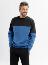Buzo de felpa con diseño de bloques de color, combinando negro en la parte superior y azul en la parte inferior y mangas. Presenta cuello redondo y puños elásticos.