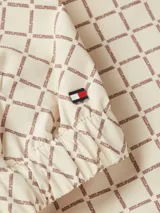 Campera deportiva Tommy Hilfiger color beige con estampado de logos en marrón. Tiene cuello alto, cierre de cremallera, dos bolsillos laterales con botones, puños elásticos y logo bordado en el puño.