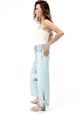 Jean de tiro alto confeccionado en denim de algodón rígido, con diseño curvo y voluminoso en las piernas, tipo barrel. Presenta cinco bolsillos, cierre frontal con botón y detalles de tiras para anudar en los tobillos.