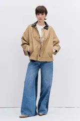 Cazadora de corte oversize en color beige, con cuello de solapa en contraste de color oscuro, cierre frontal con botones y bolsillos laterales.