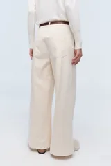 Pantalón de vestir color crema, de corte ancho y tiro alto. Se ajusta a la cintura con cinturón de cuero marrón.