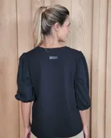 Remera blanca con cuello en V, cuerpo de algodón y mangas abullonadas de encaje bordado con puños elásticos.