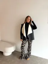 Chaleco de cuero sintético con solapas amplias forradas en corderito sintético blanco. Presenta un diseño abierto sin cierre frontal, ideal para superponer sobre vestidos.