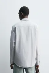 Camisa de corte regular fit confeccionada en tejido de algodón con diseño de rayas finas. Presenta cuello solapa, cierre frontal de botones y manga larga con puños abotonados.