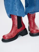 Bota tipo chelsea de cuero vacuno en color rojo con estampado floral grabado en negro. Presenta paneles laterales elásticos, suela de plataforma y taco cuadrado en color negro.