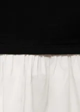 Vestido corto de diseño combinado con cuerpo negro de algodón y falda blanca con volante. Presenta cuello asimétrico, manga larga y cintura drapeada con ajuste entallado.