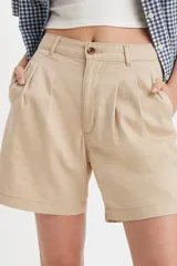 Short de corte sastrero en color beige, con diseño de pinzas frontales, cierre de botón y bragueta, y bolsillos laterales.