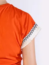 Remera color naranja de manga corta, confeccionada en algodón, con detalles de flecos y bordado en las mangas.
