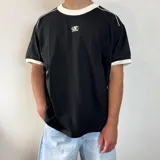 Remera de corte regular color blanco con detalles en gris oscuro en el cuello y los bordes de las mangas. Presenta un estampado pequeño centrado en el pecho.