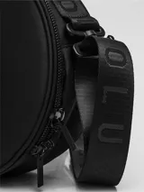 Bolso circular de estructura rígida, color negro, diseñado para el transporte de auriculares y accesorios. Cuenta con manija superior reforzada, correa de hombro ajustable con logo grabado, cierre perimetral y bolsillo trasero de acceso rápido.