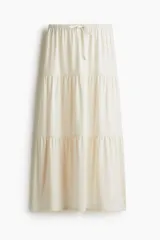Pollera maxi de tiro bajo en punto suave, con elástico revestido y cordón de ajuste en la cintura. Presenta un corte holgado con diseño de fruncido escalonado que aporta volumen y vuelo a la prenda.