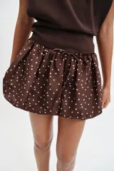 Falda pantalón de tiro medio con diseño abullonado, confeccionada en tela satinada color marrón con estampado de lunares blancos. Cuenta con cintura elástica ajustable mediante cordones.