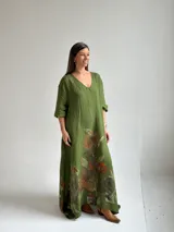 Vestido largo de lino color verde pistacho, con escote en V, mangas tres cuartos y amplio diseño holgado. Presenta un estampado floral grande y artístico en la parte inferior de la falda.