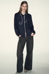 Blusa de manga larga en color azul marino, con cuello solapa y lazo frontal. Presenta detalles de pespuntes bordados en color crema a lo largo del cuello, lazo, cierre frontal y puños. Cierre frontal con botones.