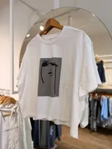 Remera blanca oversize de algodón, con cuello redondo, mangas cortas y estampa frontal en blanco y negro con diseño artístico minimalista de un rostro.
