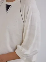 Remera de corte holgado en color crudo con sutiles rayas horizontales. Presenta mangas tres cuartos con puños elásticos, cuello redondo con detalle de costura en V y costuras decorativas oscuras en los hombros.