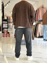 Sweater de punto liviano color beige, con textura marcada, cuello redondo y mangas largas de corte relajado, con pequeño estampado tipográfico negro en el lateral inferior.