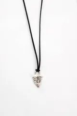 Collar con dije plateado en forma de máscara tribal, colgando de un cordón negro.