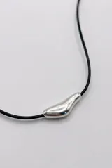 Collar largo de cordón marrón con dije colgante de metal plateado con forma orgánica y cuenta ajustable.
