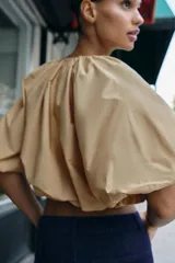 Cuerpo corto de cuello redondo con frunces, escote en pico con lazada y mangas cortas abullonadas con elástico interior.