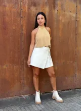 Falda corta tipo wrap de cuero color crudo, con diseño cruzado y ajuste mediante tiritas laterales.