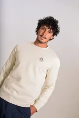 Buzo de cuello redondo color crudo, con detalle de logo bordado en el pecho, mangas largas y puños elastizados.