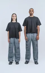 Pantalón cargo técnico gris oscuro, de silueta oversize y tejido liviano. Presenta múltiples bolsillos cargo con solapa en las piernas, uno de los cuales tiene una pequeña etiqueta negra con texto.