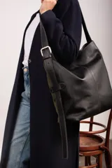 Bolso tipo bucket confeccionado en gamuza verde militar con laterales y base de cuero negro. Cuenta con una correa larga de cuero engrasado con hebilla metálica y costuras visibles en contraste.