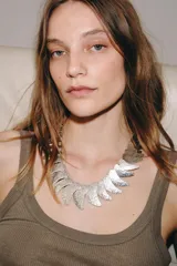 Collar de diseño statement compuesto por múltiples placas metálicas en forma de lágrima con textura rugosa, dispuestas en degradé de tamaño. Cuenta con cierre de mosquetón y cadena de ajuste.