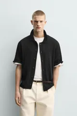 Camisa relaxed fit de punto tejida en hilatura con mezcla de algodón, color negro, con cuello solapa, manga corta y cierre frontal de botonadura.