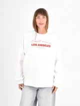 Buzo de cuello redondo y manga larga, color blanco, con estampado gráfico frontal en letras rojas que incluye la frase 'Snowfall memories LOS ANGELES'.
