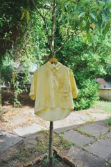 Camisa oversized de manga corta confeccionada en algodón, color amarillo con estampa artesanal de limones. Presenta un calce amplio, largo cropped con ruedo asimétrico, cuello clásico y un bolsillo frontal aplicado.