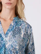 Blusa de gasa con estampado geométrico y paisley en tonos fucsia y blanco. Presenta cuello mao con escote en V, mangas tres cuartos con presilla y botón para regular el largo.
