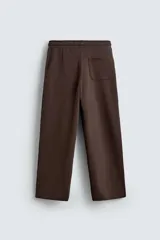 Pantalón jogger de corte relajado y pernera ancha, confeccionado en tejido de algodón con interior perchado. Cuenta con cintura elástica ajustable mediante cordón interior, bolsillos laterales y un bolsillo trasero de plastrón.