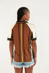 Camiseta deportiva estilo polo de color marrón con diseño estampado, cuello negro y detalles en blanco y verde flúor. Cuenta con mangas cortas y escudo frontal con las iniciales 'ETC' flanqueadas por aves.