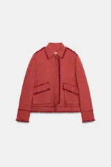 Chaqueta corta de tweed en color rojo, con cuello solapa, manga larga y bolsillos frontales con solapa. Presenta detalles deshilachados en los bordes y cierre frontal con cremallera oculta.
