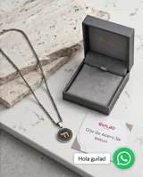 Collar con dije circular de acero inoxidable, con centro esmaltado en negro y símbolo Jai en baño de oro. Incluye cadena de eslabones tipo veneciana.