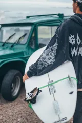 Hoodie de corte boxy fit en color negro con efecto lavado. Presenta estampado gráfico en la espalda con la frase 'Glassy Waves' en tipografía estilo fuego y detalles de llamas en las mangas.