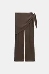 Pantalón de tiro medio con pernera recta y amplia, confeccionado en tejido con textura. Presenta una pieza superpuesta tipo pañuelo anudada en la cintura y bajo ajustable con botón.