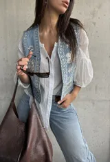 Chaleco de denim celeste con bordados detallados y apliques de brillos en la parte frontal.